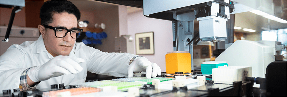 A scientist arranging microplates on the deck of a liquid handling robot
