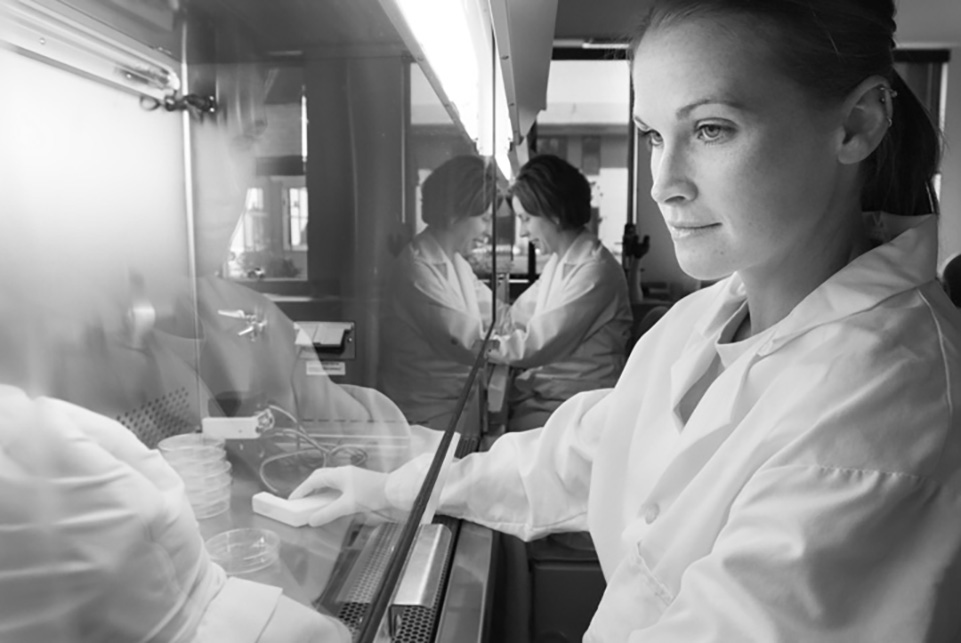  Black and white photo of a scientist sitting at a fume hood in a lab