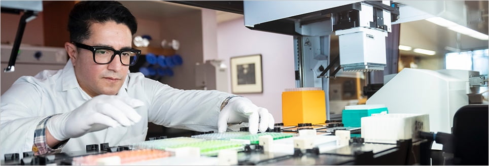 A scientist arranging microplates on the deck of a liquid handling robot